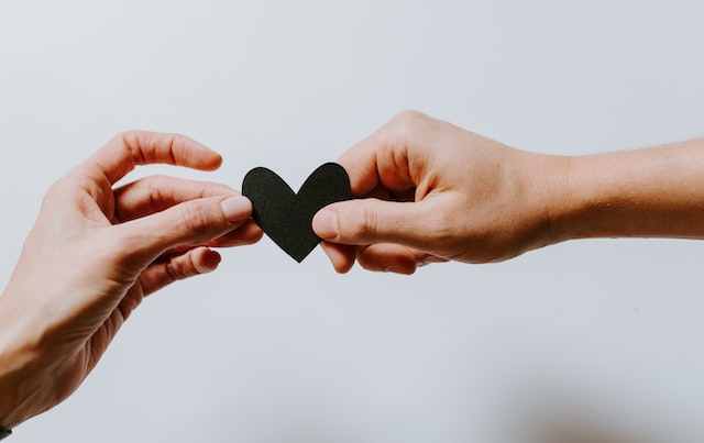 One hand handing over a paper heart to another hand.