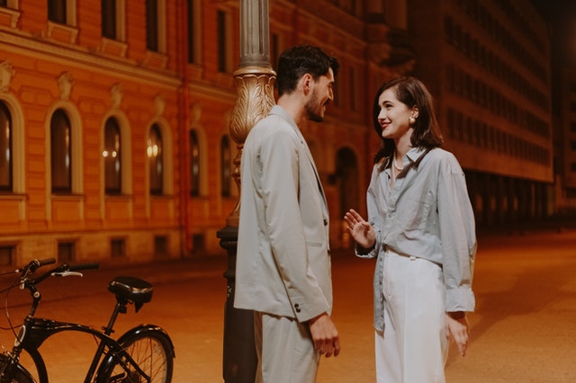 Man and woman standing in the street, smiling at each other with the women holding some distance between them