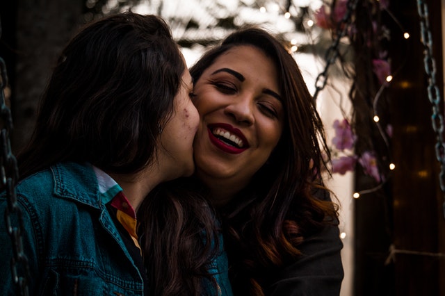 Two women sitting on swing, cuddling and smiling