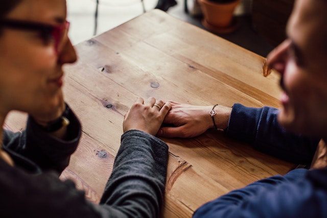 Man and woman holding hands on top of table smiling and talking