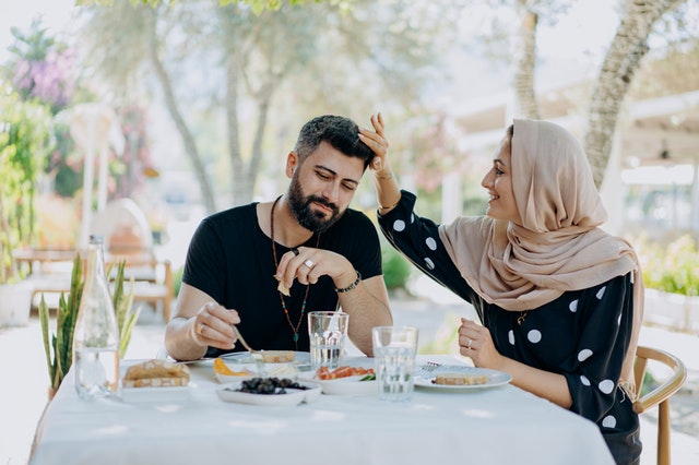 Couple sitting at a table where the woman is fixing something in the man's hair