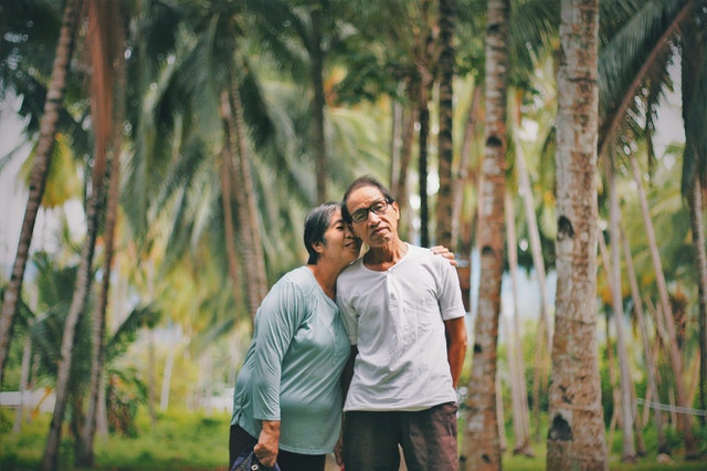 Elderly couple standing among palm trees hugging