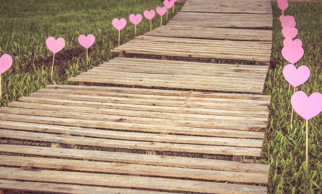 Wooden pathway on grass, framed by a row of pink hearts on either side