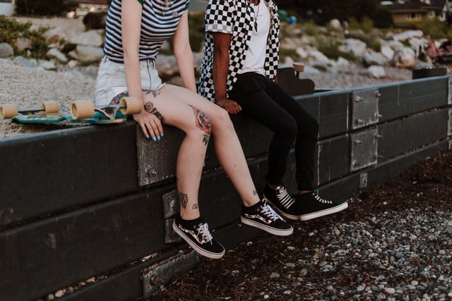 Two skateboarders sitting on a low wall next two each other