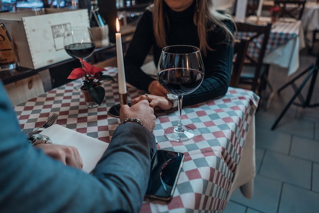 Romantic setting of two people sitting at restaurant table, holding hands with two glasses of red wine and a candle