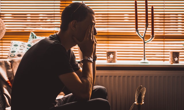 Man sitting on couch in a dark room, with his hands covering his eyes