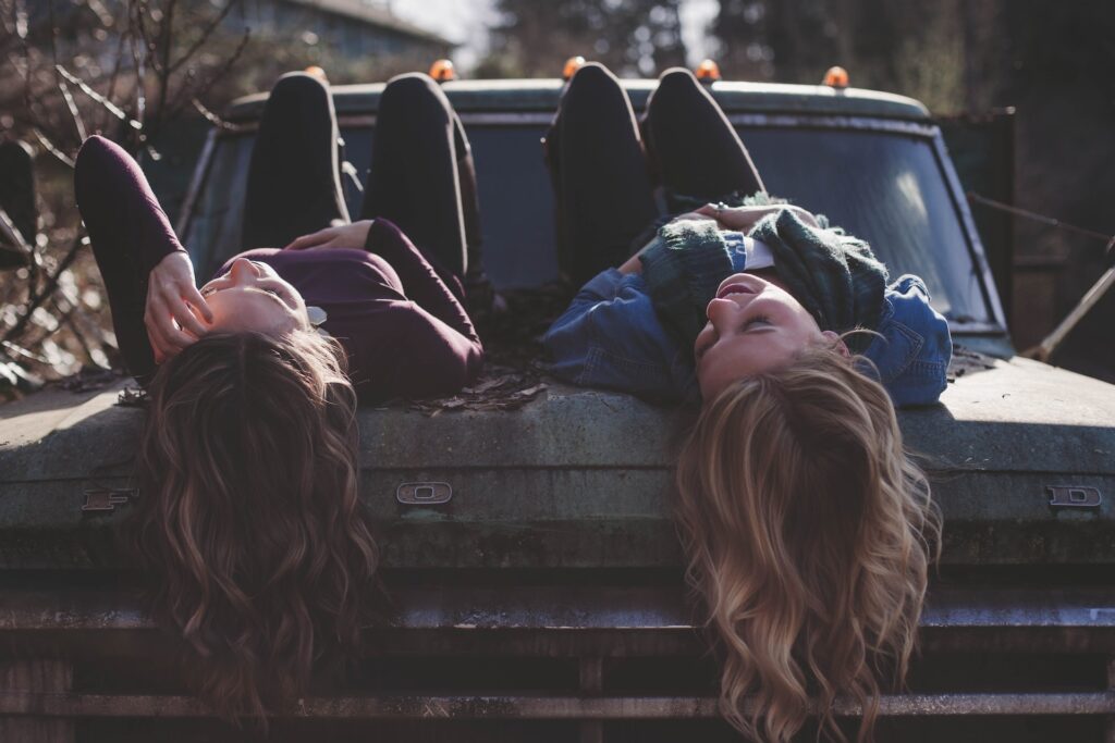 two women lying on the hood of a car looking up at the sky