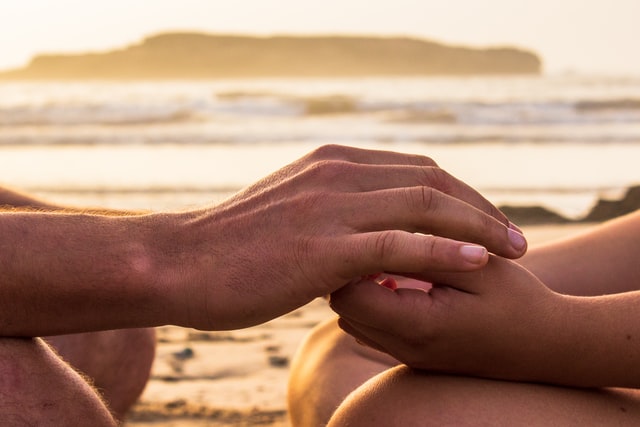 one person's hand gently holding the other's with a beach sunrise scene in the background