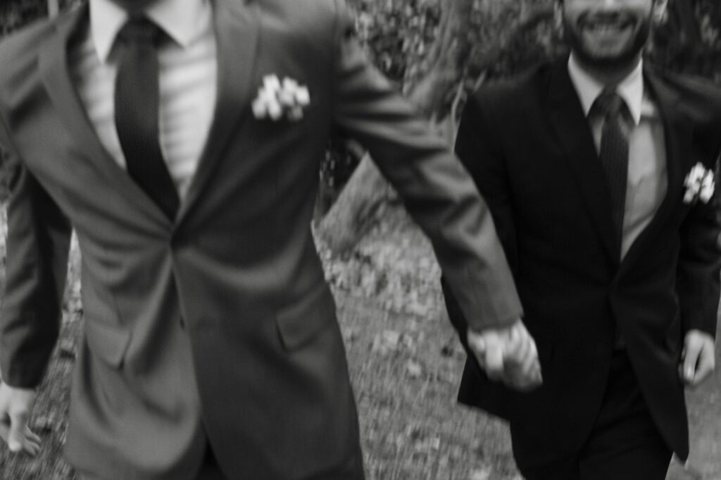 Two men in suits running hand in hand towards the camera