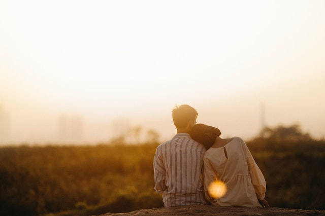 Image of a couple from the back. A woman resting her head on a man's shoulder.