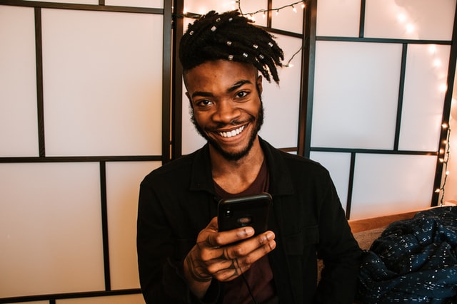 Man sitting with his phone in hand smiling at the camera